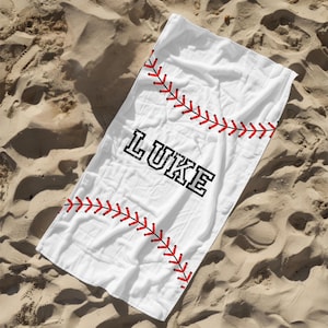 May include: White beach towel with a red baseball stitch design and the name "LUKE" in black block letters.