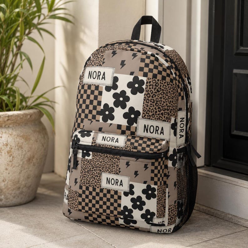 May include: A backpack featuring a patchwork design of beige, black, and white patterns including leopard print, checkerboard, lightning bolts, and flowers. The bag has multiple rectangular patches with the name NORA printed in black text.