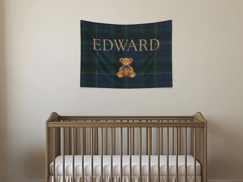 May include: A tapestry with the name "EDWARD" in tan lettering over a blue and green plaid pattern. A brown teddy bear with a blue bow tie sits below the name. A wooden crib is in the foreground.