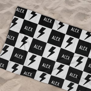 May include: Black and white checkered beach towel with a lightning bolt design and the name "ALEX" repeated throughout.