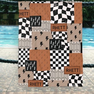 May include: A patchwork-style blanket with a mix of patterns, including black and white checkered squares, brown squares, and lightning bolt designs. The name "RHETT" is displayed on brown patches. The blanket is hanging near a pool.