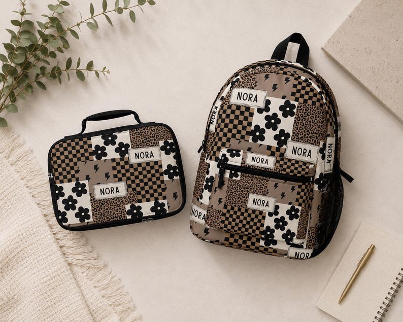 May include: A backpack and a rectangular lunch bag featuring a patchwork design of black and white flowers, brown and black checkerboard patterns, leopard print, and lightning bolts. Both items have white rectangular labels with the name NORA.
