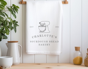 May include: White kitchen towel with a black and white illustration of a stand mixer. The text "Charlotte's Sourdough Bread Bakery" is printed below the illustration. The text "Est 2024" is printed above the illustration.