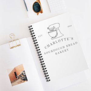 May include: A white spiral bound notebook with the text "EST 2024 CHARLOTTE'S SOURDOUGH BREAD BAKERY" and a line drawing of a stand mixer.