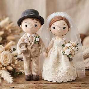 May include: Crocheted bride and groom dolls, perfect for wedding decor. The groom wears a tan suit and a gray hat, holding a ring box. The bride wears a white dress and veil, holding a bouquet. The dolls are handmade.