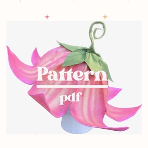 May include: A pink and white flower-shaped craft with the text "Pattern pdf". The flower has large, curved petals and green leaves. The design is set against a white background with decorative stars.