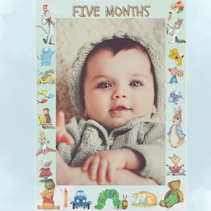 May include: A baby in a gray knitted sweater and a white knitted hat is smiling at the camera. The baby is in a photo frame with a blue background and a border of colorful illustrations from children's books. The text "FIVE MONTHS" is at the top of the frame.