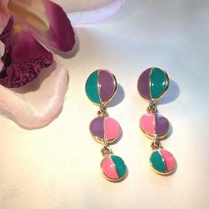 Peut inclure: Une paire de boucles d'oreilles pendantes dorées composées de trois breloques circulaires reliées verticalement. Chaque breloque est divisée en deux moitiés avec un émail coloré dans des tons violet, bleu sarcelle et rose.