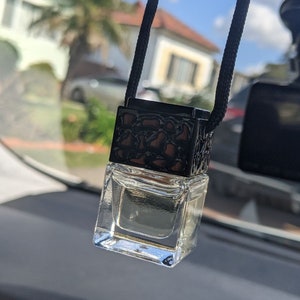 May include: A clear glass bottle with a black and gold cap hanging from a black string. The bottle is filled with a clear liquid and is likely a car air freshener.