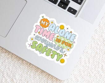 May include: A die-cut sticker featuring the text MY ALONE TIME IS FOR EVERYONE'S SAFETY in a multi-colored, bubble-style font. The design includes small yellow smiley faces, white daisies, and colorful starbursts on a white background.