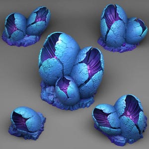 Peut inclure: Plusieurs sculptures fantastiques représentant des œufs bleus fissurés avec des surfaces texturées. Les intérieurs sont d'un violet vibrant. Les sculptures sont montées sur une base texturée violette, créant une esthétique unique et d'un autre monde.