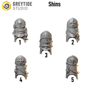 May include: An image displays five gray shin armor designs. Each piece features intricate details, including skulls, crosses, and chains. The text "Shins" is above the armor pieces, and the logo for "GREYTIDE STUDIO" is in the upper left corner.