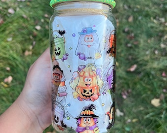 Peut inclure: Un bocal en verre transparent avec un couvercle en paillettes vertes. Le bocal est décoré sur le thème d'Halloween avec des personnages de dessins animés habillés en costumes. Les personnages incluent un fantôme, une citrouille, une sorcière et une momie.