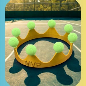 May include: A gold-colored crown with eight green tennis balls as its points, resting on a tennis court. The crown has the letters "MVP" engraved on the front. The background shows a tennis net and trees.