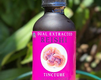 May include: A dark brown glass bottle with a dropper top, labelled "Dual Extracted Reishi Tincture Stress Support". The label is pink with a white circle containing a red and white mushroom.