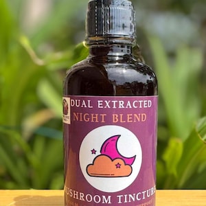 May include: A glass bottle with a dropper filled with a dark liquid. The label is purple and says "Dual Extracted Night Blend Mushroom Tincture". It also says "Calm | Immune | Sleep Support" and "Suggested Use: 1 serving up to 3x daily or as needed". The bottle is sitting on a wooden surface.