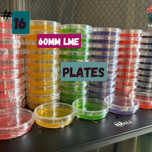 May include: Stacks of clear, round petri dishes filled with colorful liquids. The text "60MM LME PLATES" is visible. The dishes are arranged on a black shelf, with a logo in the upper right corner.