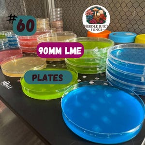 May include: A collection of clear, round petri dishes filled with colorful liquids, including blue, green, and yellow. The dishes are stacked and arranged on a black surface. Text on the image reads "#60", "90MM LME", and "PLATES". A logo for "Needle Juice Fungi" is also visible.