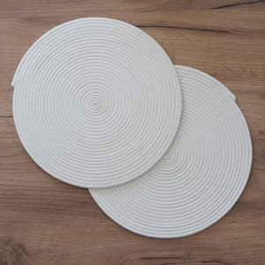May include: Two white round woven placemats with a circular pattern.