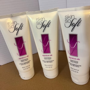 May include: Three white tubes of Skin So Soft Signature Silk replenishing hand cream. Each tube has the brand name in a script font, a purple rectangle with a white design, and the text "crème régénératrice pour les mains".