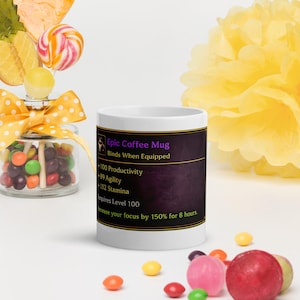 Könnte beinhalten: Ein weißer Keramik-Kaffeebecher mit einem violetten Grafikfeld und goldenem Rand. Der Text lautet: Epic Coffee Mug, Binds When Equipped, +100 Productivity, +89 Agility, +112 Stamina, Requires Level 100, Increase your focus by 150% for 8 hours.