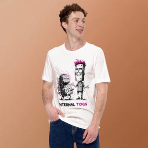 May include: A white short-sleeved t-shirt featuring a graphic illustration of a character with pink hair standing next to a smoking, mechanical box-like creature. The text "INTERNAL TOOS" is printed in black and pink below the illustration.