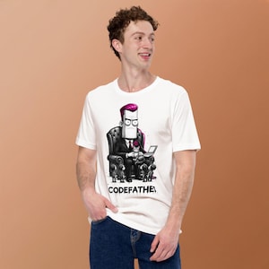 May include: A white t-shirt featuring a graphic illustration of a character with magenta hair sitting in a leather chair, holding a cat and a laptop, surrounded by small figures. The text CODEFATHER is printed in black at the bottom of the graphic.