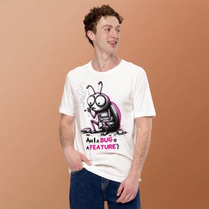 Op de afbeelding: Een wit T-shirt met korte mouwen en een afbeelding van een cartoon-insect dat rookt en een fles vasthoudt. Het insect is omringd door flessen en de tekst eronder luidt "AM I A BUG OR A FEATURE?" in zwarte en roze letters op de voorkant.