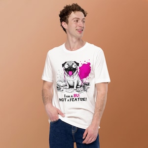 May include: A white short-sleeve t-shirt featuring a graphic of a pug with a pink cloud behind it. The pug has its tongue out. Below the graphic, the text reads: I AM A BUG, NOT A FEATURE! The design includes scattered debris like shoes and paper.