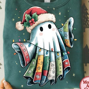 Könnte beinhalten: Grünes Sweatshirt mit einem Cartoon-Geist, der einen Weihnachtsmannhut und ein Outfit im Patchwork-Stil trägt. Der Geist ist mit einer Lichterkette geschmückt. Das Design ist festlich und skurril, ideal für die Weihnachtszeit.