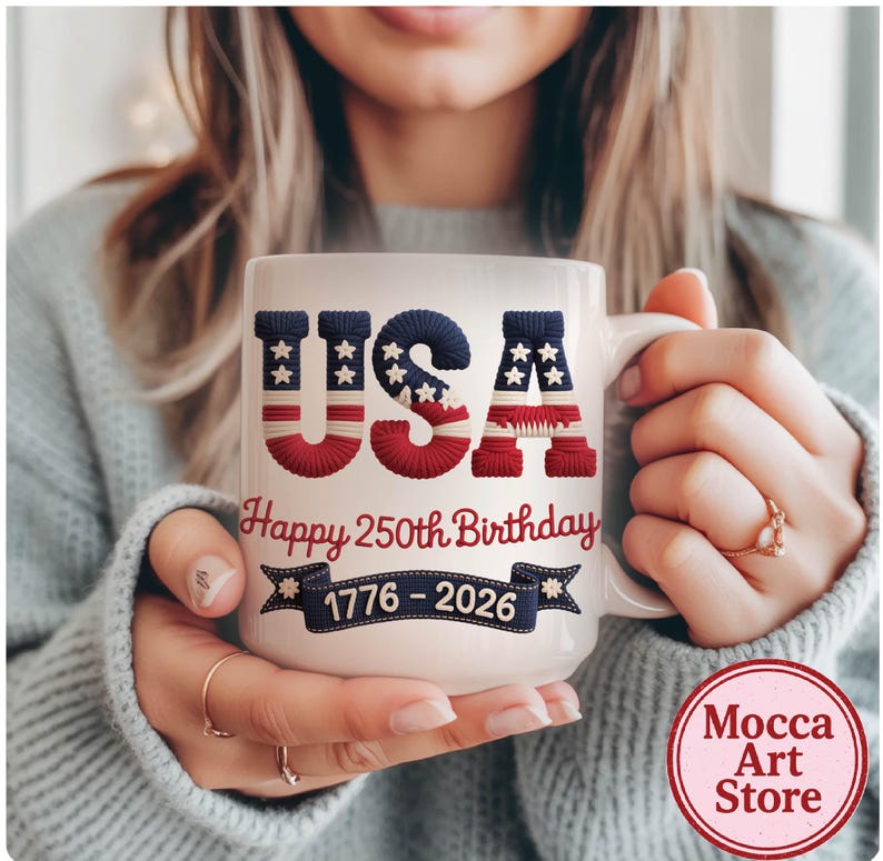May include: White ceramic mug featuring the word "USA" in red, white, and blue, with a stars and stripes design. The mug also has the text "Happy 250th Birthday" and "1776-2026". The mug is held by a person.