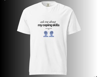 May include: White t-shirt featuring the text "ask me about my coping skills" in black, and a blue graphic of two heads connected by a line. The shirt also has the text "since therapy became cool".