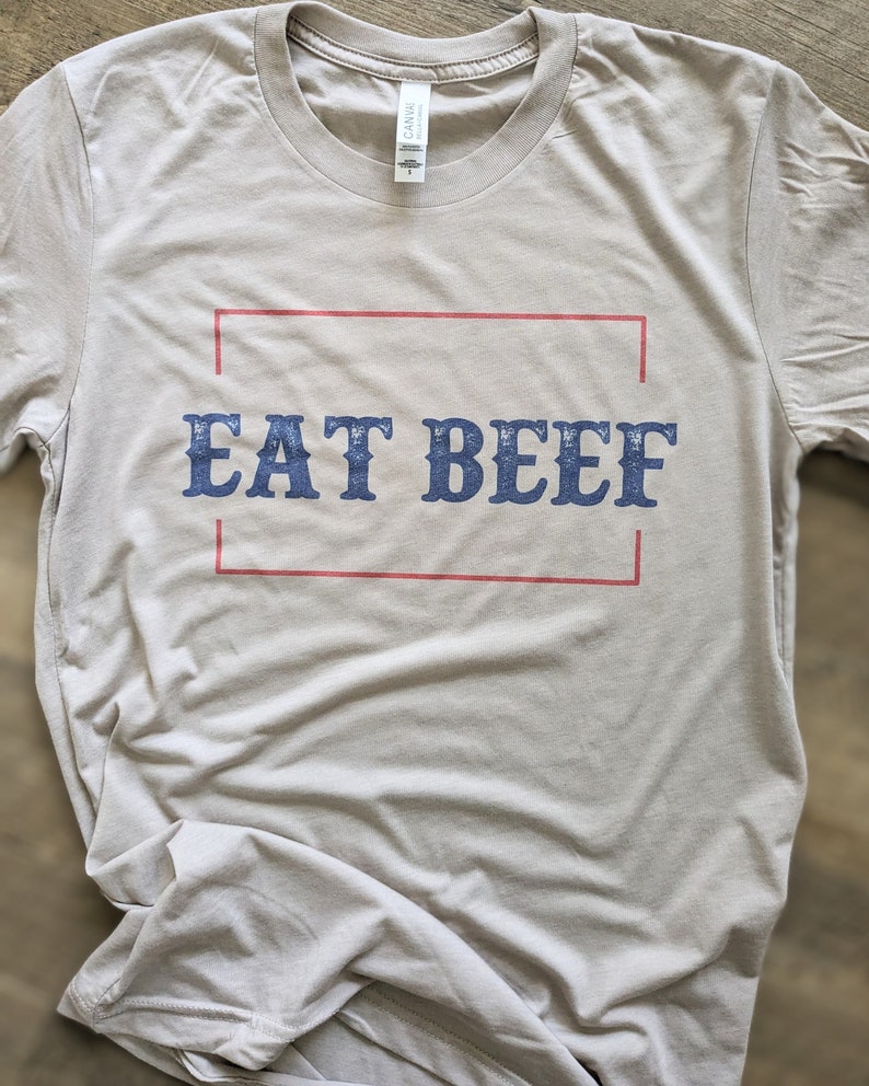 May include: A light gray t-shirt with a red and white border around the text "EAT BEEF" in blue.