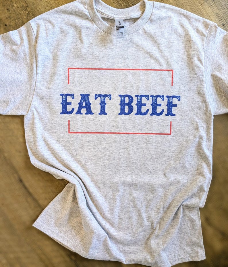 May include: A gray t-shirt with the text "EAT BEEF" printed in blue letters inside a red rectangle.
