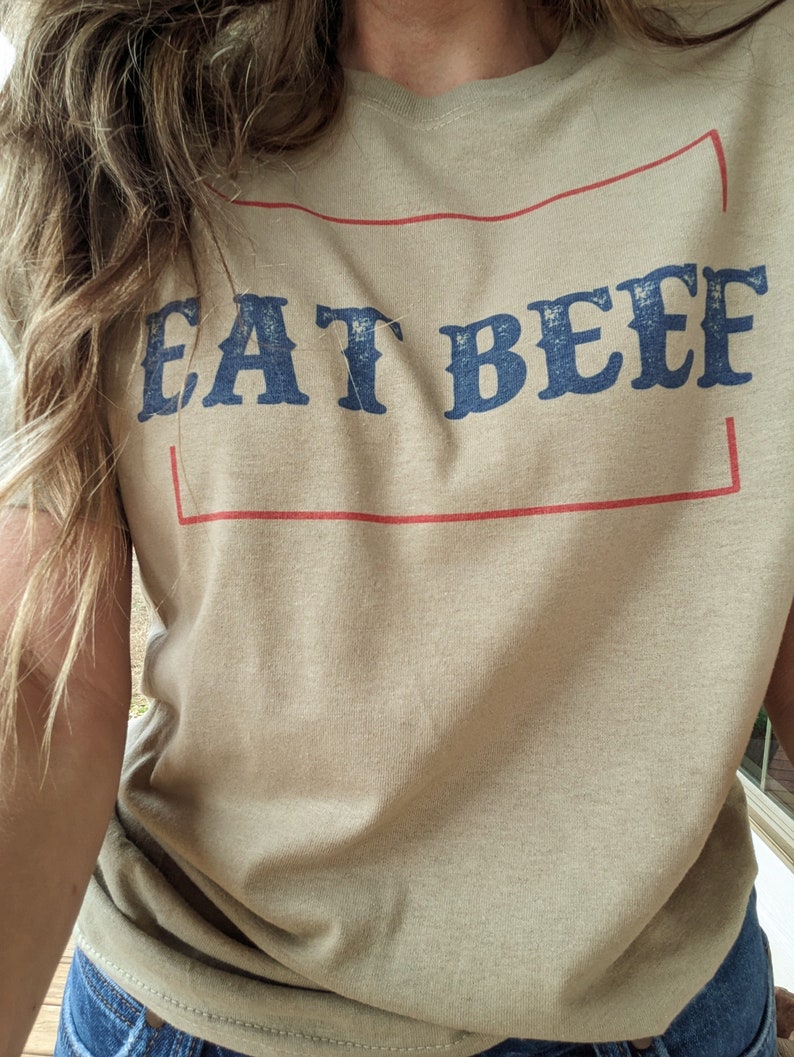 May include: A tan t-shirt with a red rectangle around the text "EAT BEEF" in blue lettering.