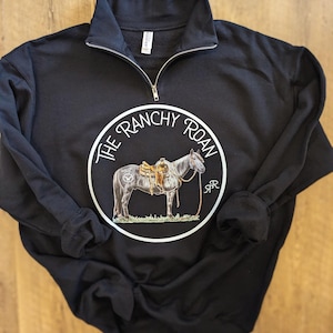 May include: Black sweatshirt with a white circle graphic featuring a horse with a saddle and the text "The Ranchy Roan" in a white circle.