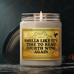 Op de afbeelding: Een witte kaarsenpot met een gouden label waarop staat "Smells Like It's Time To Read Fourth Wing Again". De kaars is een sojawaskaars en weegt 9 oz en brandt 50 uur. Hij is handgemaakt in Californië.