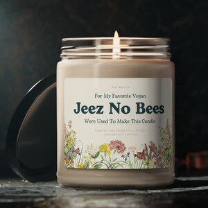 May include: A lit soy wax candle in a clear glass jar with a black lid. The label reads "Jeez No Bees" with floral illustrations. The candle is hand-poured in California and has a 255g volume.