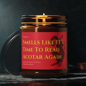 Peut inclure: Un bocal en verre brun contenant une bougie avec une étiquette rouge sur laquelle est inscrit "Smells Like It's Time To Read ACOTAR Again". La bougie est allumée et l'étiquette présente un motif de dragon.