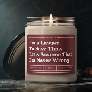 May include: A clear glass jar candle with a silver lid, featuring a burgundy label with the text "I'm a Lawyer. To Save Time, Let's Assume That I'm Never Wrong." The candle is 9 oz and hand-poured in California.