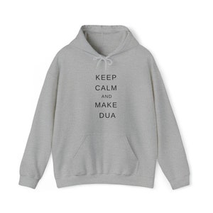 May include: A light gray hoodie with a drawstring hood and a front pocket. The text "KEEP CALM and MAKE DUA" is printed in black, centered on the front. The hoodie is made of a soft, comfortable material.