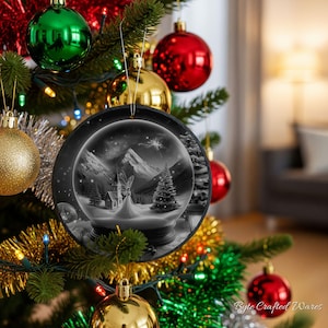 May include: A round black Christmas ornament featuring a monochrome illustration of a snow-covered landscape with a church, a fairy, and pine trees inside a glass globe. The ornament hangs from a silver string on a decorated evergreen tree.