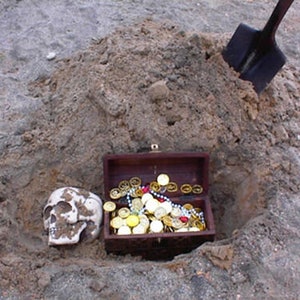 May include: A wooden treasure chest filled with gold coins and beads is buried in the sand. A skull is next to the chest and a shovel is partially visible in the background.