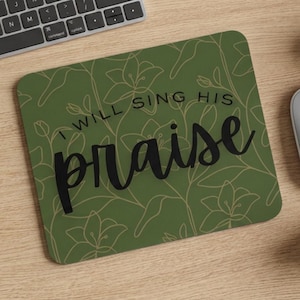 May include: A square mouse pad with rounded corners featuring an olive green background, a thin gold-colored line art floral pattern, and the black text "I WILL SING HIS praise" written in a combination of serif and script fonts.