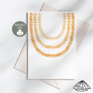 Può includere: Una scheda stampabile bianca con tre fili di ghirlande floreali arancioni. La scheda ha il testo "PRINTABLE CARD" e un'icona della stampante in un cerchio grigio. La scheda è sopra una busta bianca.