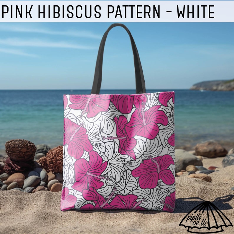 Puede incluir: Una bolsa de tela blanca con un patr&oacute;n de flores de hibisco rosas. La bolsa tiene asas negras y est&aacute; sentada en una playa con rocas y arena.