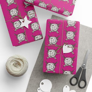 May include: Gift wrap featuring a repeating pattern of white dice with swords on a magenta background. The wrapped gifts are tied with twine and have white tags. A ball of twine, scissors, and tags are also visible.
