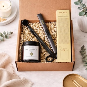 May include: A gift box containing a black candle jar with the text "Smells Like The Tears Of My Players", a black wick trimmer, a gray electric lighter, and a candle lighter box. The box is filled with shredded paper.