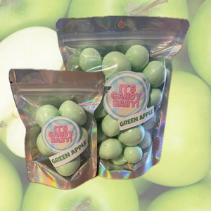 May include: Two bags of green apple flavored candy. The bags are clear and have a holographic finish. The candy is in the shape of small balls. The bags have a sticker on them that says "It's Candy Baby!" and "Green Apple".