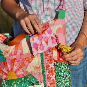 Op de afbeelding: Een kleurrijke patchwork tote bag met een bijpassend klein etui met ritssluiting. De tas heeft verschillende patronen, waaronder vlinders, bloemen en geometrische vormen in roze, oranje, groen en geel. Het kleine etui heeft een roze ijsjespatroon.